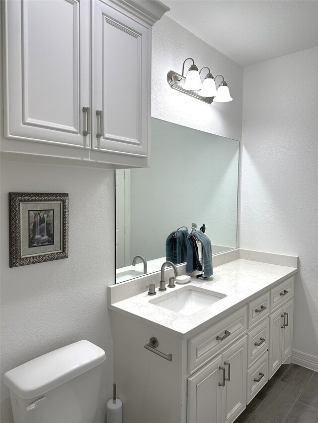 bathroom with toilet, a textured wall, and vanity