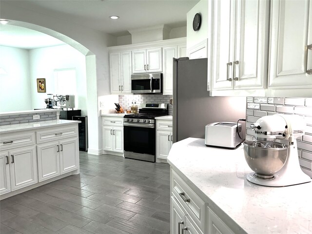 kitchen with arched walkways, dark wood-style flooring, stainless steel appliances, backsplash, and white cabinets