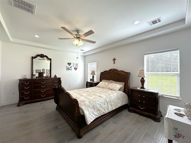 bedroom with a tray ceiling, light wood-type flooring, and visible vents