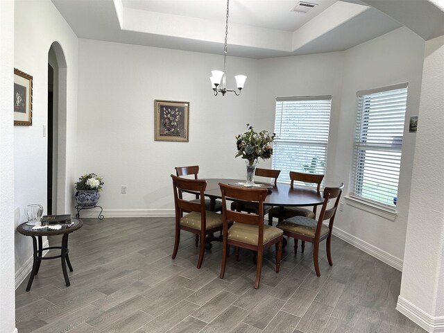 dining room featuring arched walkways, wood finished floors, a raised ceiling, and baseboards