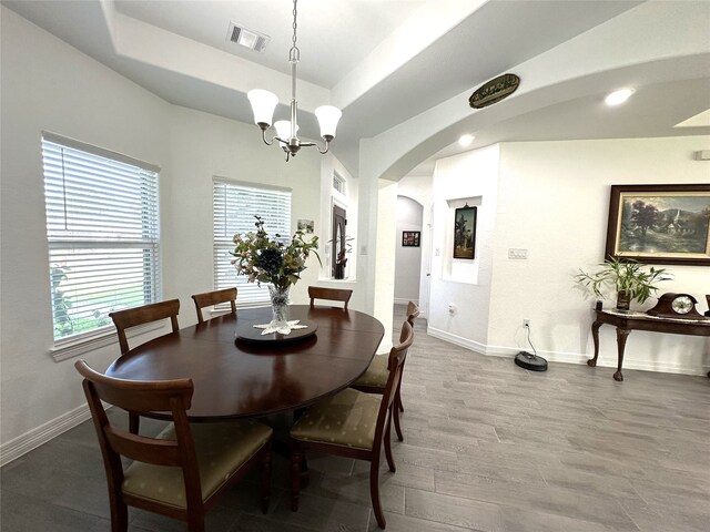 dining room with arched walkways, wood finished floors, visible vents, baseboards, and a tray ceiling