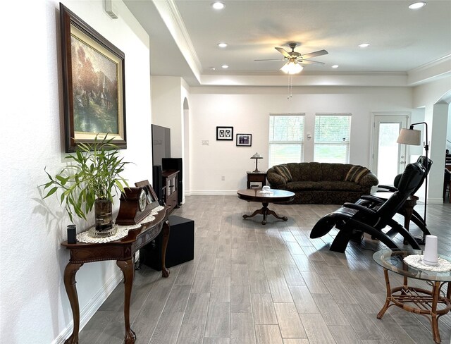 living area with arched walkways, wood finished floors, baseboards, ornamental molding, and a raised ceiling