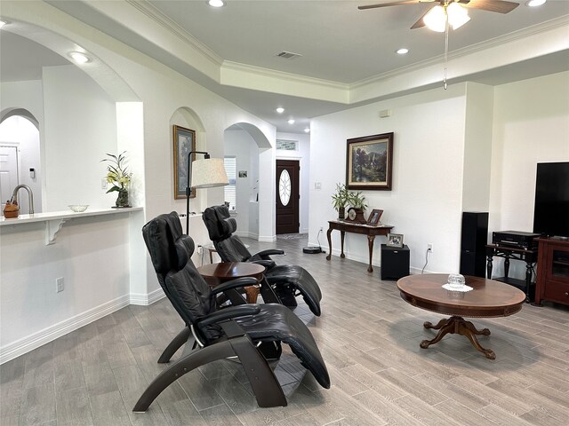 living room featuring baseboards, a raised ceiling, light wood-style flooring, crown molding, and recessed lighting