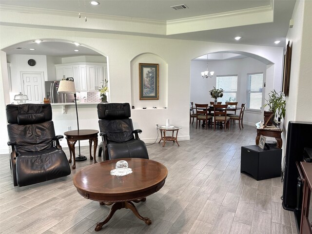 living area featuring visible vents, arched walkways, a tray ceiling, crown molding, and light wood-type flooring