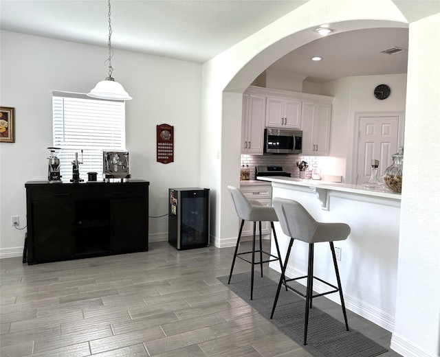 kitchen with white cabinetry, wine cooler, decorative backsplash, a breakfast bar, and appliances with stainless steel finishes