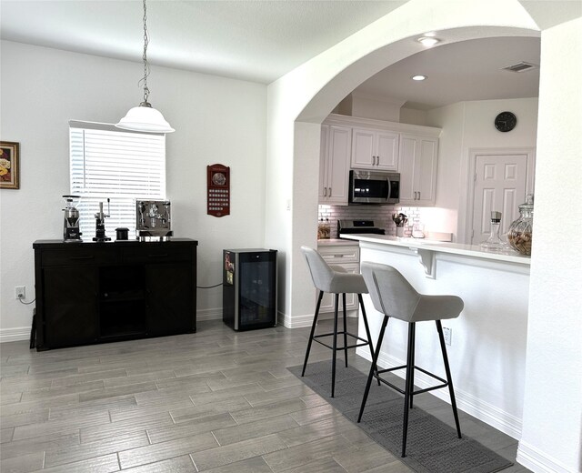 kitchen with arched walkways, wine cooler, stainless steel appliances, a breakfast bar, and visible vents