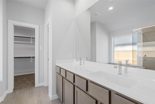 full bathroom featuring visible vents, a shower stall, a walk in closet, double vanity, and a sink