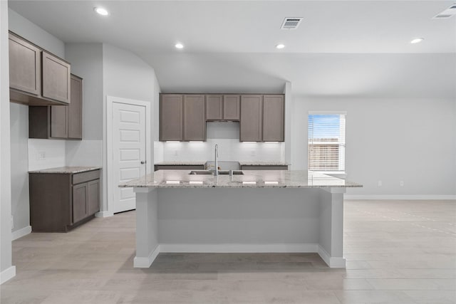 kitchen featuring a center island with sink, tasteful backsplash, visible vents, and lofted ceiling