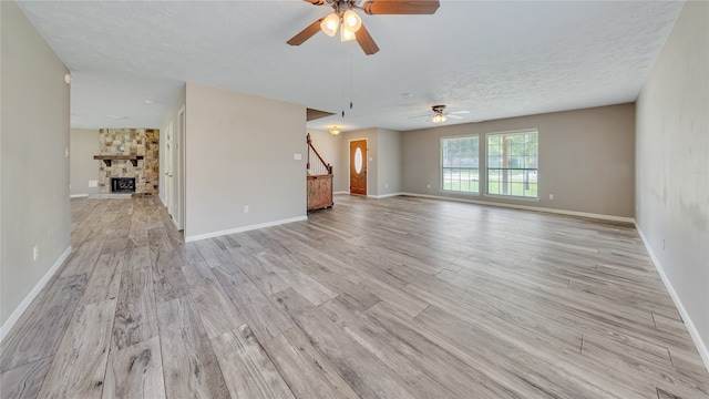 unfurnished room featuring a stone fireplace, light hardwood / wood-style flooring, ceiling fan, and a textured ceiling