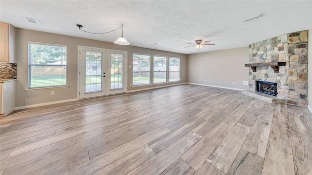 unfurnished living room with light wood-type flooring, ceiling fan, a fireplace, and a textured ceiling