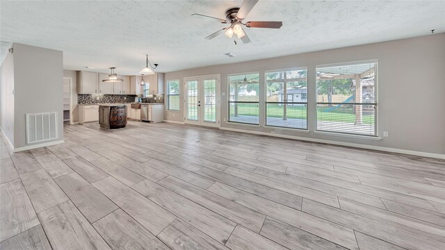 unfurnished living room featuring ceiling fan, a textured ceiling, and light hardwood / wood-style flooring