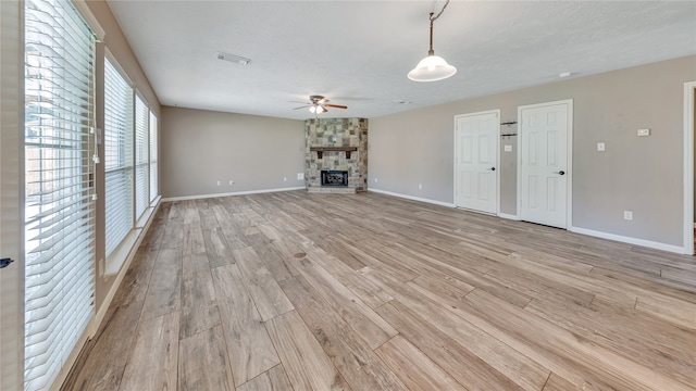 unfurnished living room with a textured ceiling, ceiling fan, a stone fireplace, and light wood-type flooring