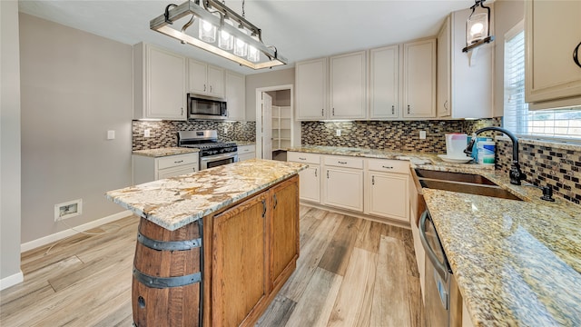 kitchen with light wood-type flooring, tasteful backsplash, stainless steel appliances, light stone counters, and hanging light fixtures