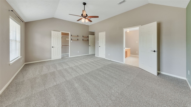 unfurnished bedroom featuring ceiling fan, a closet, vaulted ceiling, a walk in closet, and light colored carpet