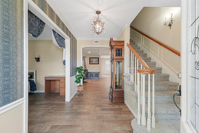 entryway with a textured ceiling, light hardwood / wood-style floors, a notable chandelier, and ornamental molding