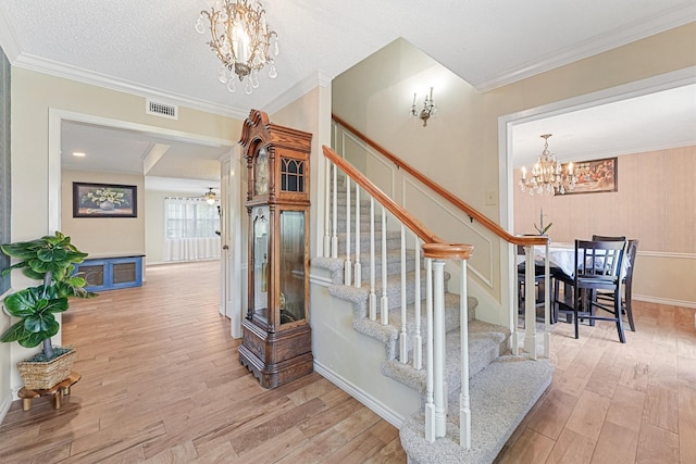 staircase featuring crown molding, visible vents, an inviting chandelier, a textured ceiling, and wood finished floors