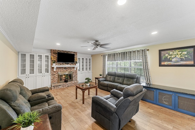 living room featuring a textured ceiling, a brick fireplace, ceiling fan, and light hardwood / wood-style floors