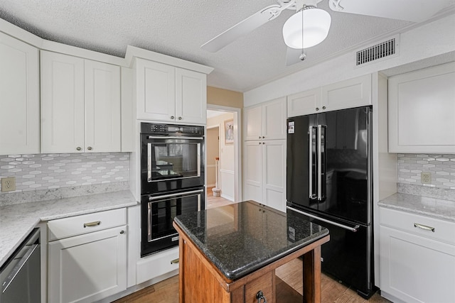 kitchen with light stone counters, white cabinetry, visible vents, light wood-style floors, and black appliances