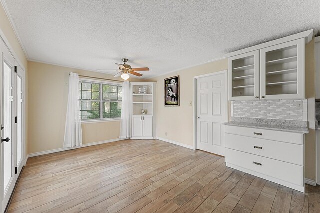 unfurnished living room with light wood-type flooring, a textured ceiling, ornamental molding, and ceiling fan