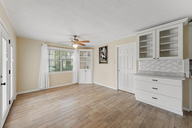 interior space with a textured ceiling, light wood finished floors, a ceiling fan, and baseboards