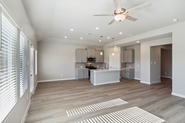 kitchen featuring tasteful backsplash, hanging light fixtures, appliances with stainless steel finishes, gray cabinets, and a kitchen island with sink