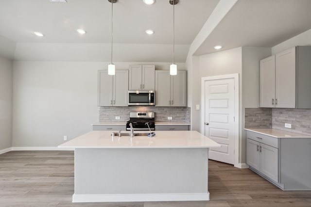 kitchen with pendant lighting, stainless steel appliances, a kitchen island with sink, and gray cabinetry