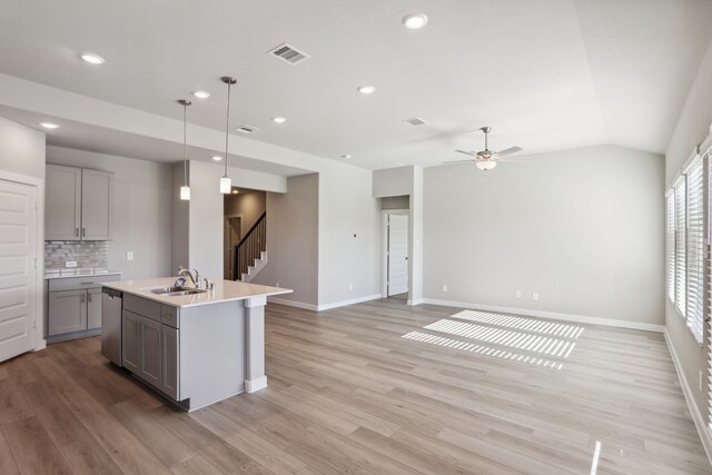 kitchen featuring sink, gray cabinets, a kitchen island with sink, decorative light fixtures, and light wood-type flooring