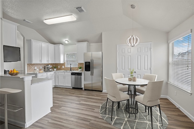 kitchen featuring light hardwood / wood-style flooring, backsplash, hanging light fixtures, appliances with stainless steel finishes, and white cabinets