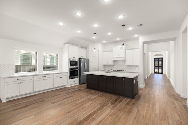 kitchen featuring white cabinets, light wood-type flooring, stainless steel appliances, and an island with sink