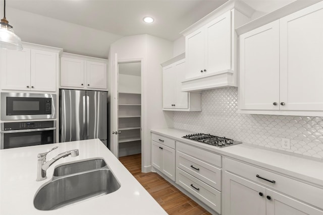 kitchen with pendant lighting, sink, hardwood / wood-style flooring, white cabinetry, and stainless steel appliances