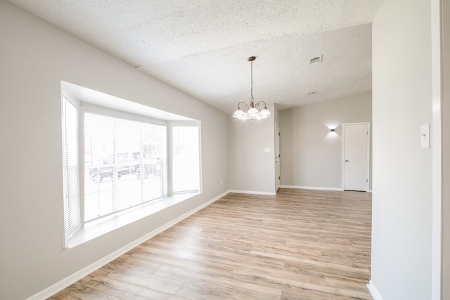 spare room with a textured ceiling, light hardwood / wood-style flooring, and a notable chandelier