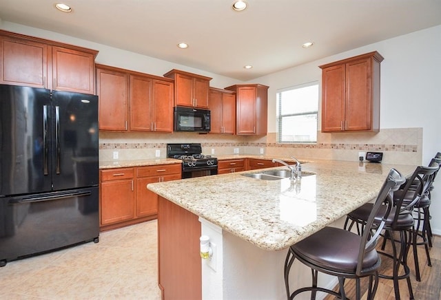 kitchen featuring light stone countertops, black appliances, a breakfast bar, sink, and decorative backsplash