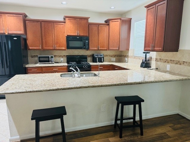 kitchen featuring black appliances, light stone countertops, decorative backsplash, and dark hardwood / wood-style flooring