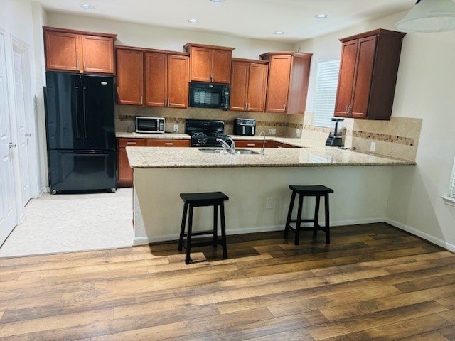 kitchen featuring black appliances, a kitchen breakfast bar, hardwood / wood-style flooring, and backsplash