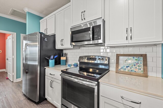 kitchen featuring appliances with stainless steel finishes, ornamental molding, light hardwood / wood-style floors, and white cabinetry