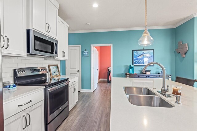 kitchen with sink, white cabinets, hanging light fixtures, appliances with stainless steel finishes, and hardwood / wood-style floors