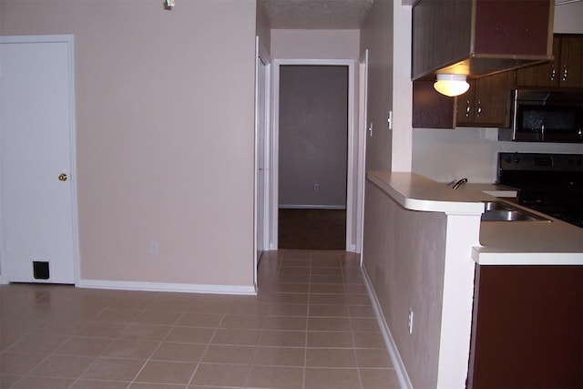 kitchen featuring dark brown cabinetry, light tile patterned floors, kitchen peninsula, and range with electric cooktop