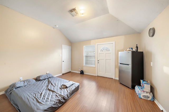 bedroom with light hardwood / wood-style floors, stainless steel refrigerator, and vaulted ceiling