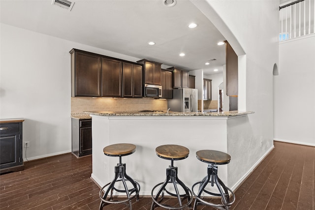 kitchen with light stone countertops, dark wood-type flooring, stainless steel appliances, kitchen peninsula, and decorative backsplash