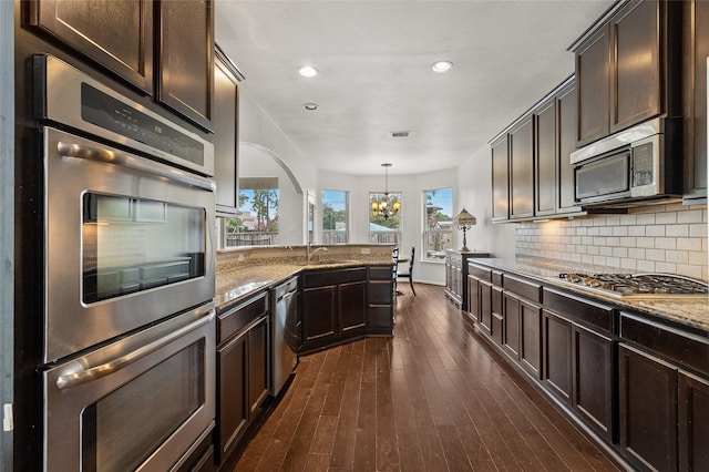 kitchen with dark hardwood / wood-style floors, decorative light fixtures, stainless steel appliances, decorative backsplash, and light stone counters