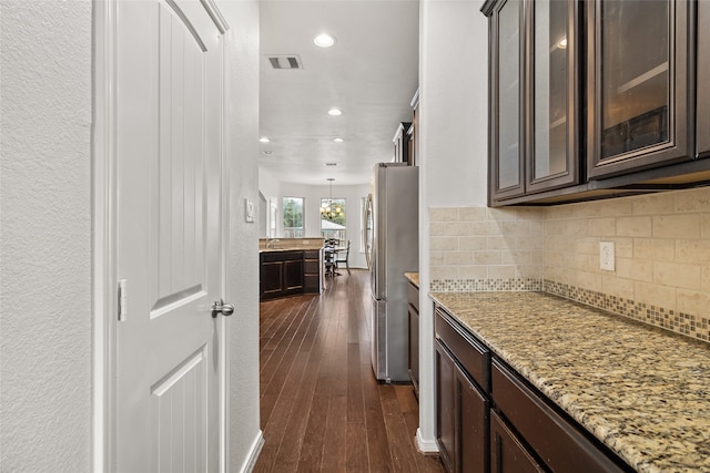 kitchen featuring light stone counters, stainless steel fridge, dark hardwood / wood-style floors, dark brown cabinets, and tasteful backsplash