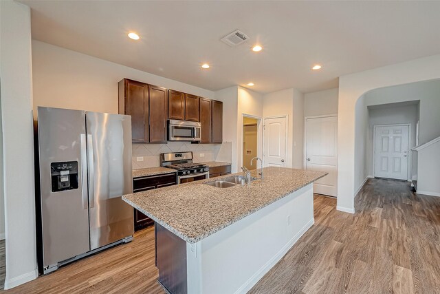 kitchen featuring light wood-type flooring, backsplash, sink, appliances with stainless steel finishes, and a center island with sink