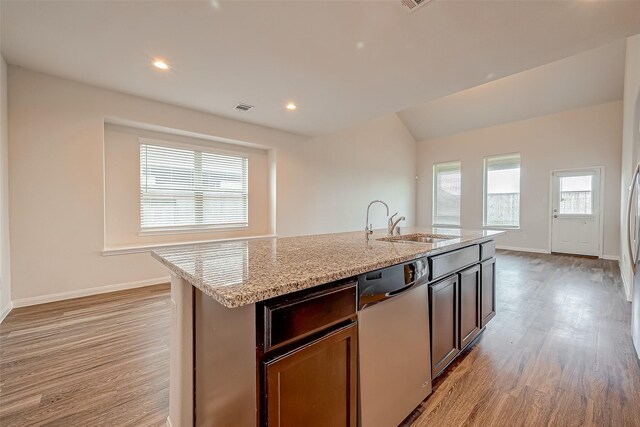 kitchen featuring dishwasher, light stone counters, an island with sink, sink, and light hardwood / wood-style floors