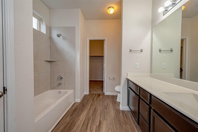 full bathroom with wood-type flooring, toilet, tiled shower / bath, and vanity