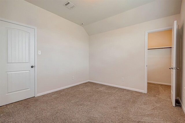 unfurnished bedroom featuring a walk in closet, a closet, light carpet, and vaulted ceiling