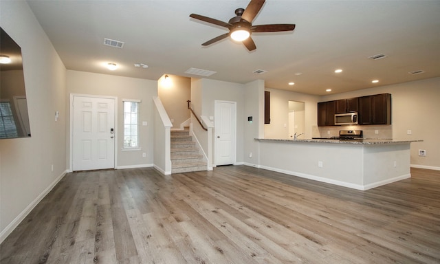 kitchen featuring appliances with stainless steel finishes, hardwood / wood-style floors, ceiling fan, and light stone countertops