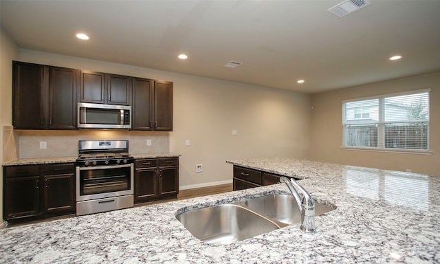 kitchen featuring appliances with stainless steel finishes, light stone counters, backsplash, and sink