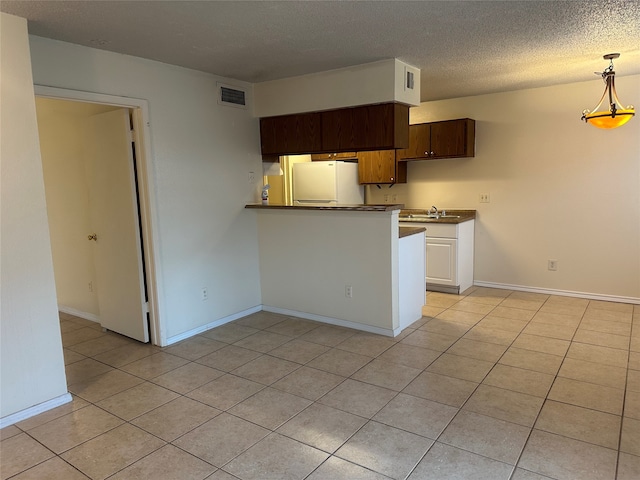 kitchen with white fridge, a textured ceiling, light tile patterned floors, kitchen peninsula, and sink