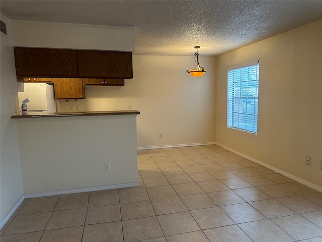 kitchen featuring a textured ceiling, kitchen peninsula, light tile patterned floors, and white fridge