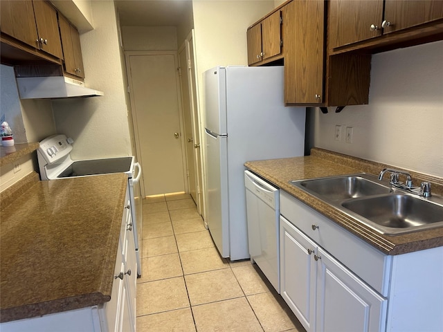 kitchen featuring a sink, under cabinet range hood, light tile patterned floors, white appliances, and dark countertops